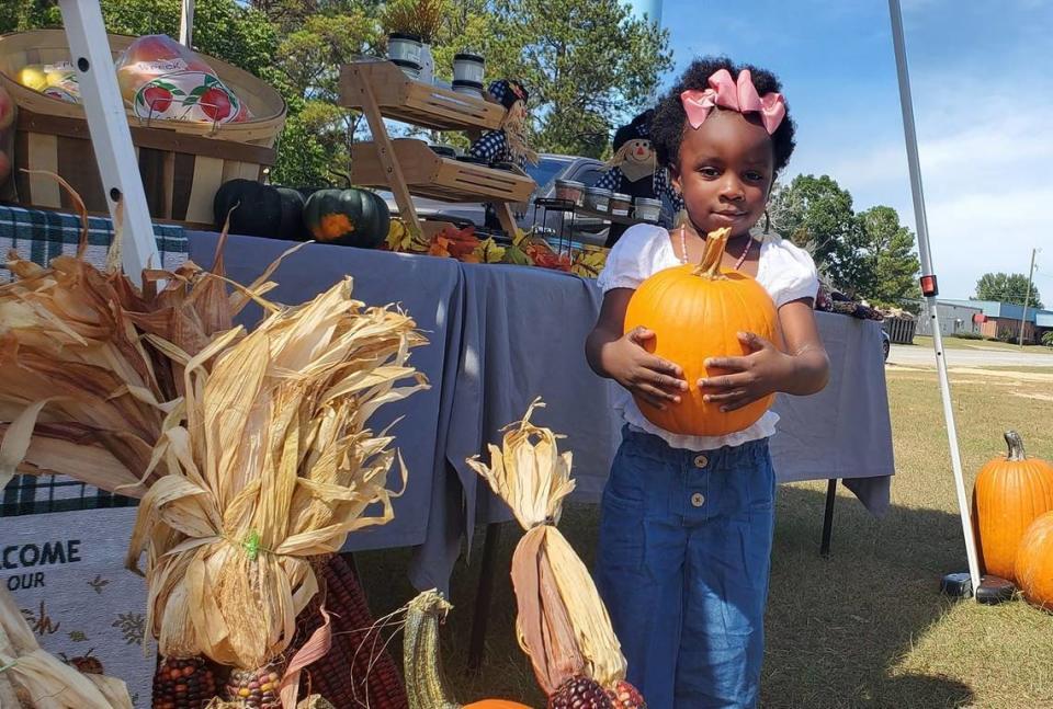 A young girl carries a pumpkin at the International City Farmers Market in Warner Robins. The market helps feed the homeless thanks to owner Joshua Hess.