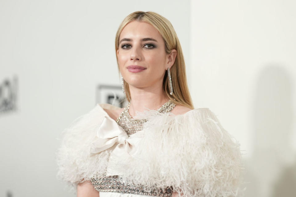 Emma Roberts on the red carpet, wearing an elegant dress with feather detailing and silver jewelry