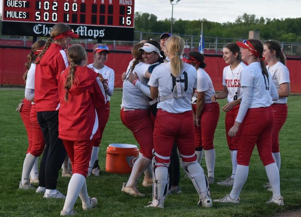 Bedford softball coach Marla Gooding is surrounded by her players after reaching 100 career victories during a sweep of Novi on Friday, May 10, 2024.