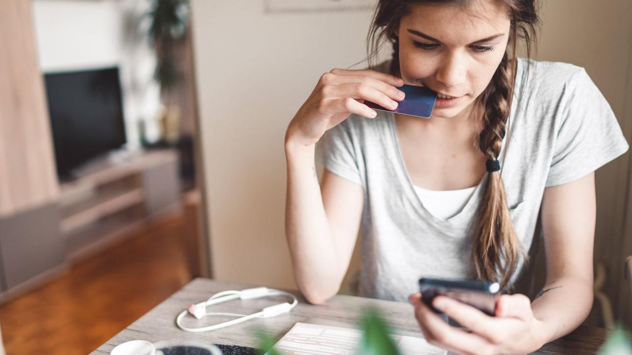 Young woman with braided hair sitting by the table, looking on her smart phone.