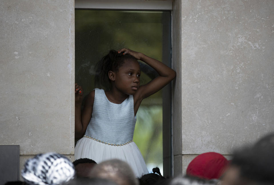 A girl sits on an outer window ledge of the U.S. Embassy in Port-au-Prince, Haiti, Friday, July 9, 2021. A large crowd gathered outside the embassy amid rumors on radio and social media that the U.S. will be handing out exile and humanitarian visas, two days after Haitian President Jovenel Moïse was assassinated in his home. (AP Photo/Fernando Llano)
