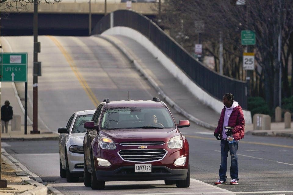 Shamonte Jones, right, talks to a commuter while offering to wash the windshield of their vehicle in exchange for cash, Tuesday, Jan. 10, 2023, in Baltimore. Local officials are rolling out their latest plan to steer squeegee workers away from busy downtown intersections and toward formal employment using law enforcement action and outreach efforts. On Tuesday, police started enforcing anti-panhandling laws in six zones where squeegeeing is most common. (AP Photo/Julio Cortez)