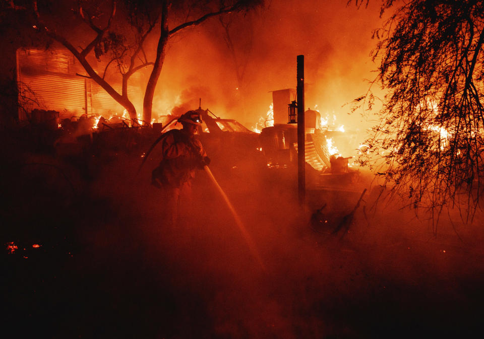 A firefighter takes a hose to a burning property while battling the Fairview Fire Monday, Sept. 5, 2022, near Hemet, Calif. (AP Photo/Ethan Swope)