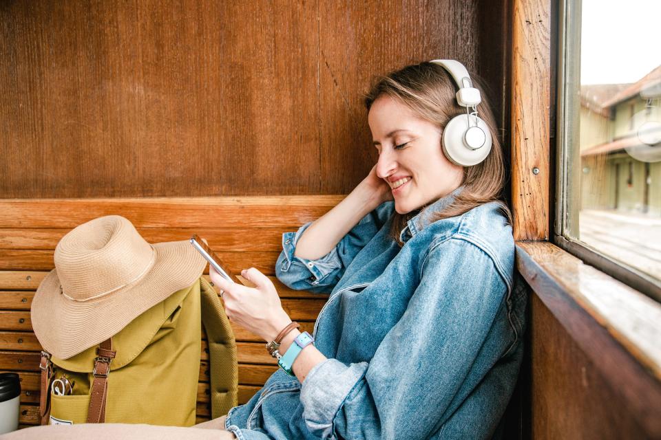 A woman in a train wearing headphones and using a smart phone.