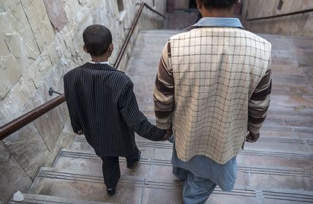 Waqas,12, who contracted HIV through a tainted blood transfusion, walks down a flight of stairs with his father after an interview with Reuters in Islamabad December 5, 2014. REUTERS/Zohra Bensemra