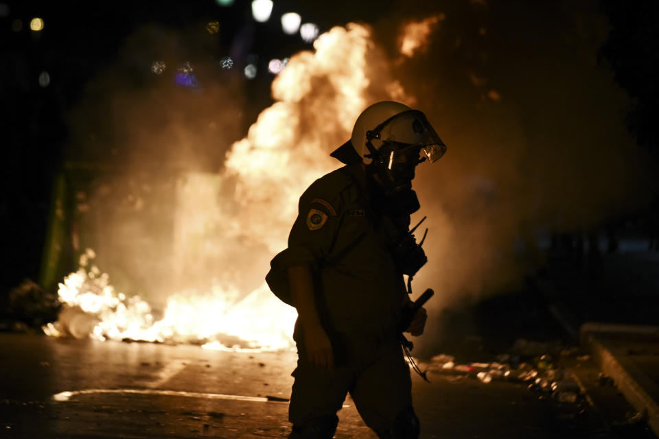 CORRECTING TO REMOVE REFERENCE TO ALLEGIANCE OF GROUP CLASHING WITH POLICE - A police officer walks in front of burning garbage cans during clashes with protesters in the northern Greek city of Thessaloniki, Saturday, Sept. 8, 2018. Police in northern Greece have clashed with protesters outside an international trade fair where prime minister Tsipras made a keynote speech. (AP Photo/Giannis Papanikos)