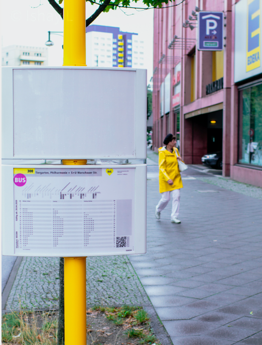 A woman appears to accessorise with this yellow bus stop pole in Berlin.