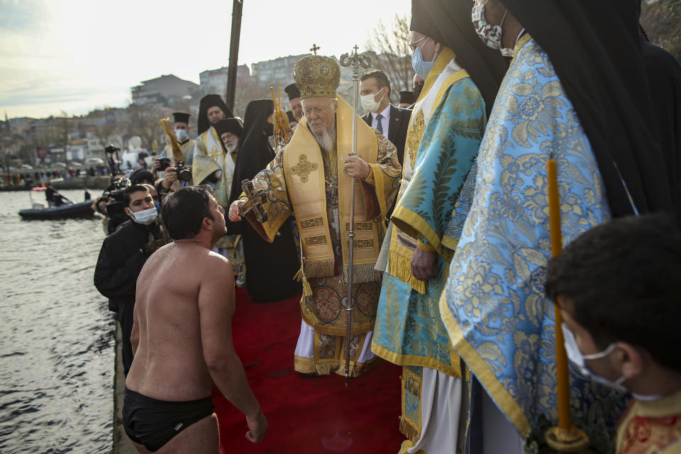 Ecumenical Patriarch Bartholomew I, the spiritual leader of the world's Orthodox Christians, hands out a wooden crucifix to a faithful that jumped into the waters of the Golden Horn to retrieve it, during the Epiphany ceremony in Istanbul, Wednesday, Jan. 6, 2021. With no visiting faithful from Greece or other Christian Orthodox countries, due to the coronavirus pandemic, only two swimmers raced to retrieve the cross in a ceremony commemorating the baptism of Jesus Christ. (AP Photo/Emrah Gurel)