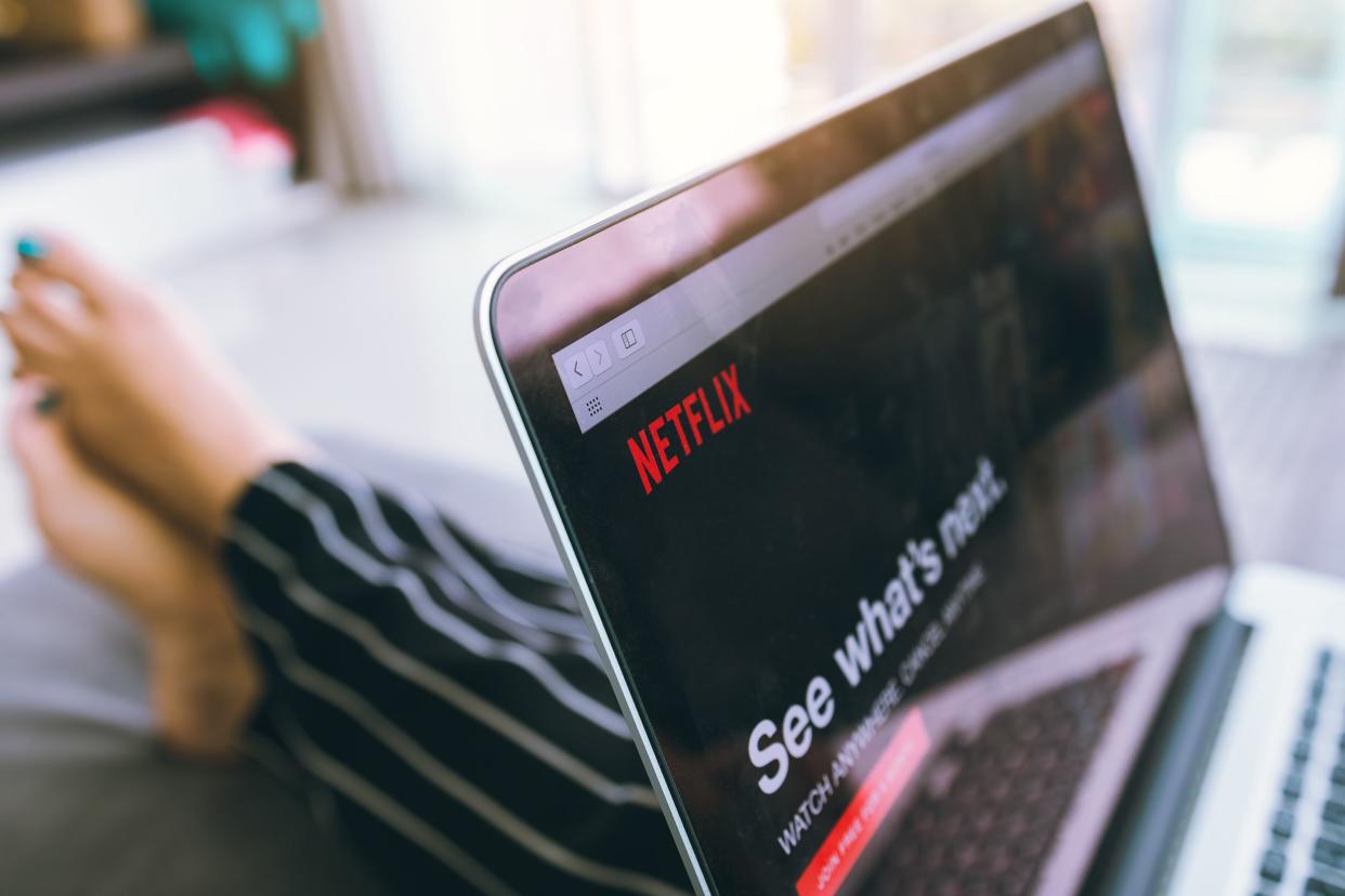 Closeup of Netflix website in Safari brower on a laptop screen, selective focus, blurred background of a legs laying on a bed with the bedroom in the background