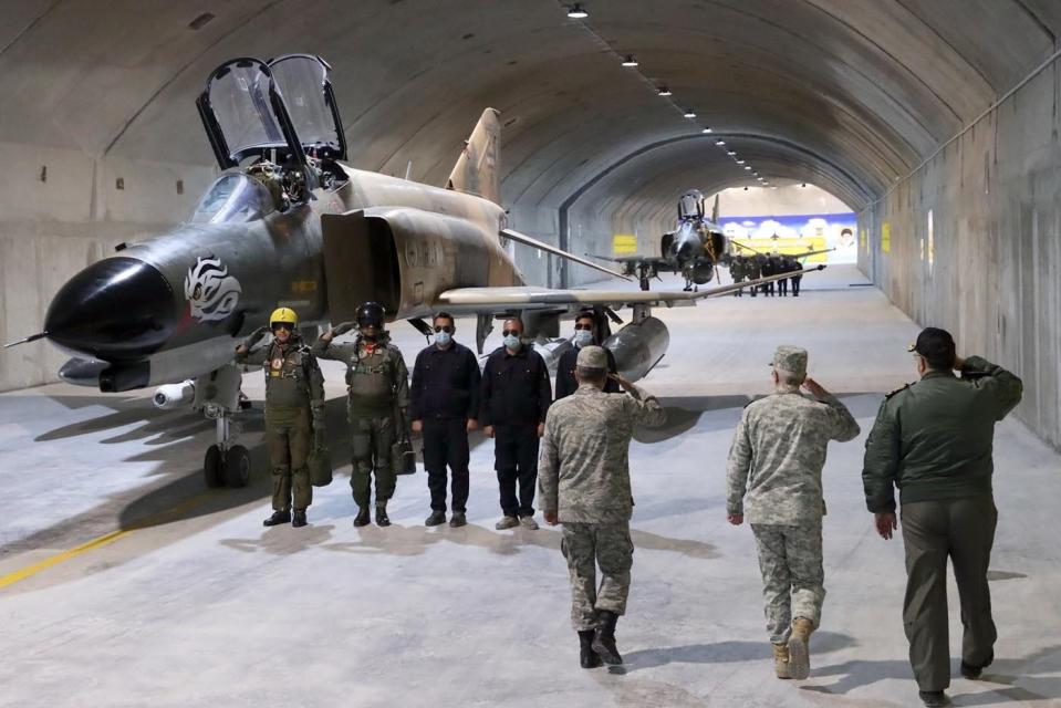 An underground tunnel with an aircraft and military officials walking past.