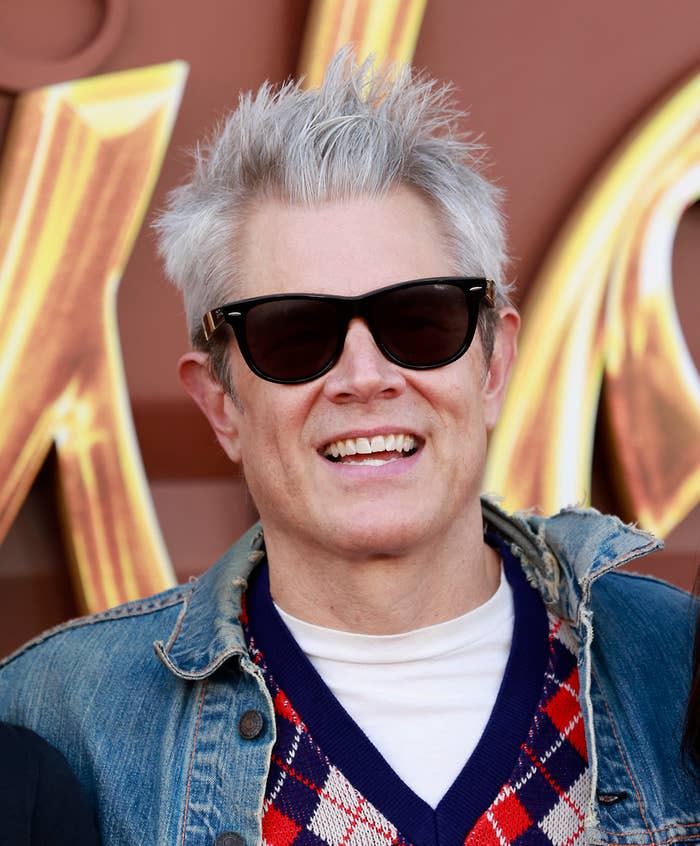 closeup of him in a denim jacket and sunglasses smiling at a daytime event