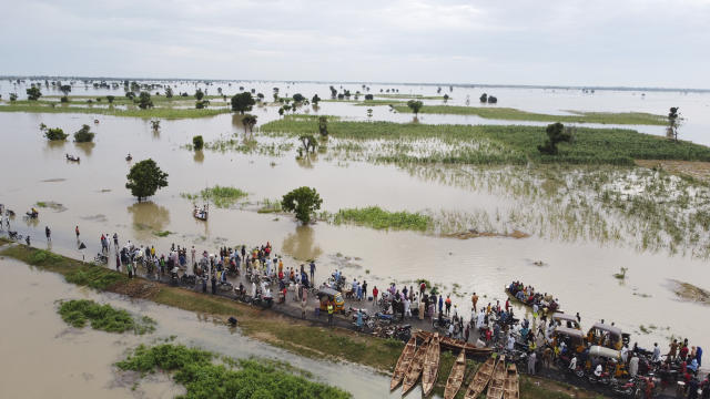 FILE - People walk through floodwaters near flooded farmlands after heavy rainfall in Hadeja, Nigeria, Sept 19, 2022. During a conference in the Ethiopian capital of Addis Ababa on Monday, March 20, 2023, leaders of African countries hit hard by climate change discussed finance options that would allow for the forgiveness of debt in exchange for investment in green energies. (AP Photo, file)