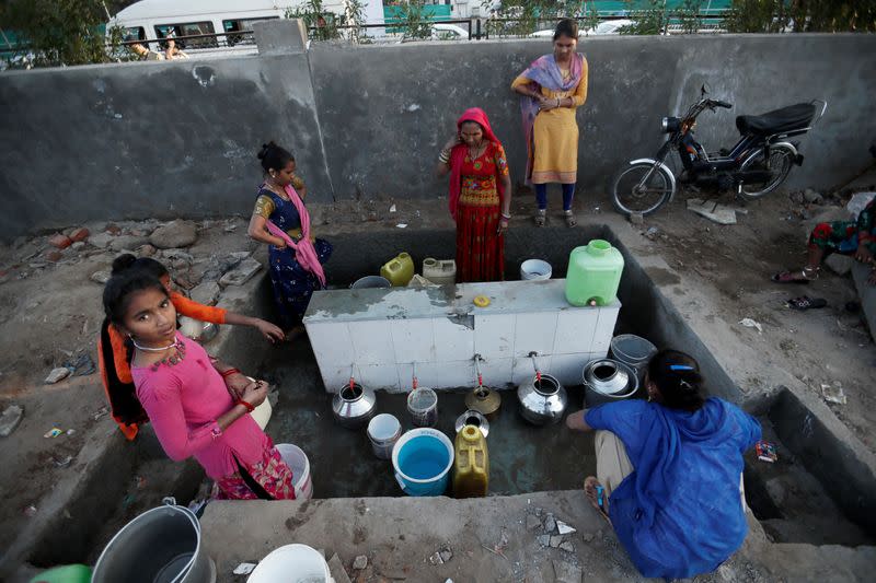 Women fill water from a tap in front of a wall constructed as part of beautification works for U.S. President Donald Trump's visit, in Ahmedabad