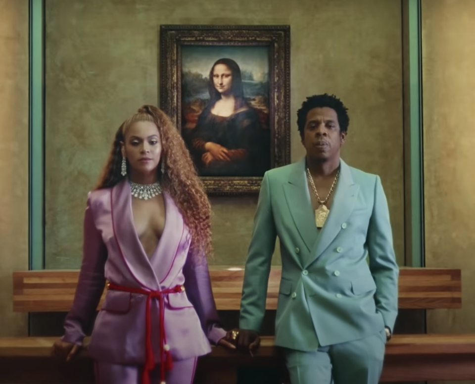 the two wearing satin suits standing in front of the mona lisa