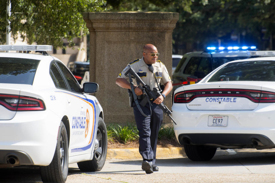 A Baton Rouge City Constable's Office officer with a weapon walks near two LSU police vehicles and Constables Office units parked in between the LSU Student Union and Coates Hall,during investigation of a possible armed intruder in Coates Hall, Tuesday, August 20, 2019.(Travis Spradling/The Advocate via AP)