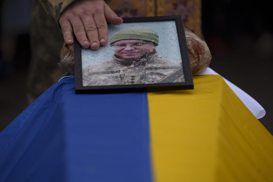 Military priest Dmytro Prysiazhnyi touches the photo of Ukrainian Cpt. Serhii Vatsko during his funeral in Boiarka, Ukraine, Friday, March 29, 2024. Vatsko, who was killed on the frontline of eastern Ukraine on March 24 joined the country's military in 2014. (AP Photo/Vadim Ghirda)