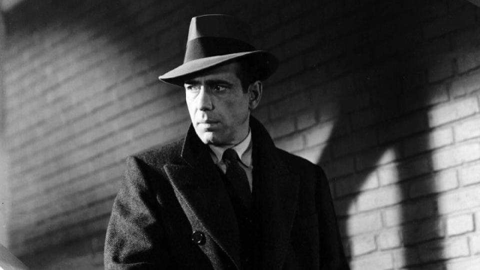 Humphrey Bogart as Sam Spade glowers in front of a brick wall with dark shadows in The Maltese Falcon