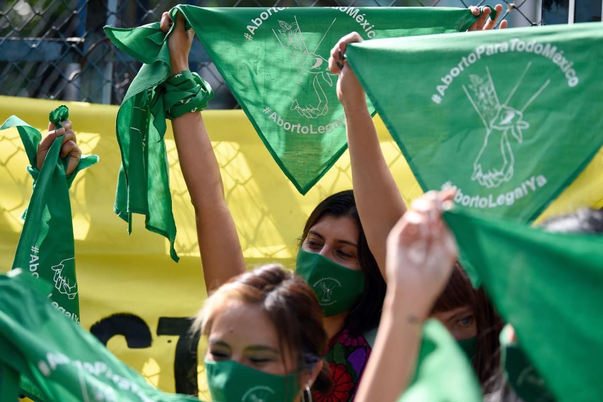 A group of women hold up green bandanas that read "Aborto legal ya," and "Aborto para todo México" or "Legal abortion now," "Abortion for all of Mexico." 