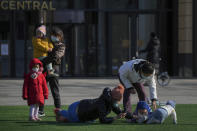 Residents with their children and toddlers play on the green outside a reopened mall in Beijing, Sunday, Dec. 4, 2022. China on Sunday reported two additional deaths from COVID-19 as some cities move cautiously to ease anti-pandemic restrictions amid increasingly vocal public frustration over the measures. (AP Photo/Andy Wong)