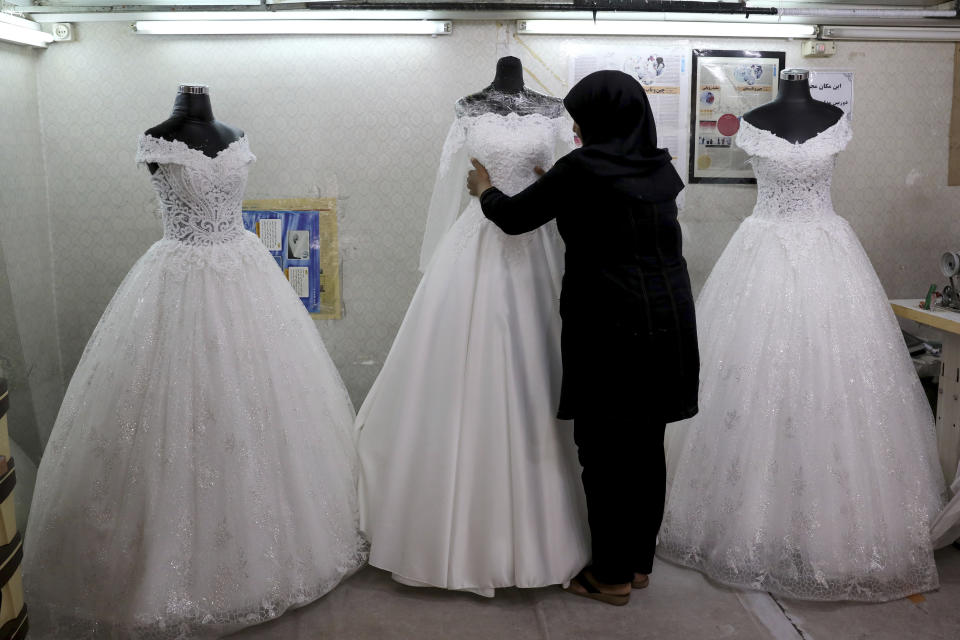 In this July 3, 2019 photo, a worker adjusts a display of wedding dresses in downtown Tehran, Iran. Iran’s large middle class has been hit hard by the fallout from unprecedented U.S. sanctions, including the collapse of the national currency. Perhaps most devastating has been the doubling of housing prices. More newlyweds move in with their families to save money. (AP Photo/Ebrahim Noroozi)