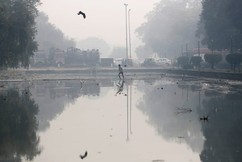 A man cleans a pond on a smoggy morning in New Delhi