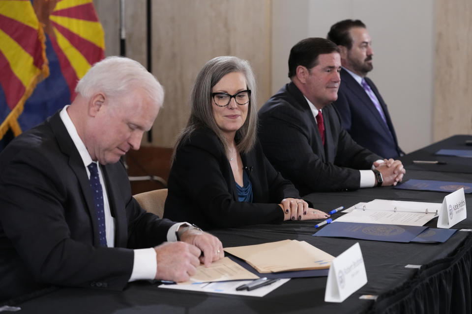 Arizona Supreme Court Chief Justice Robert Brutinel, left, signs the official Arizona general election canvass document as Katie Hobbs, the Democratic governor-elect and current secretary of state, second from left, looks on while Arizona Republican Gov. Doug Ducey, second from right, and Arizona Attorney General Mark Brnovich, right, sit at the table as well during a signing ceremony at the Arizona Capitol in Phoenix, Monday, Dec. 5, 2022. (AP Photo/Ross D. Franklin, Pool)