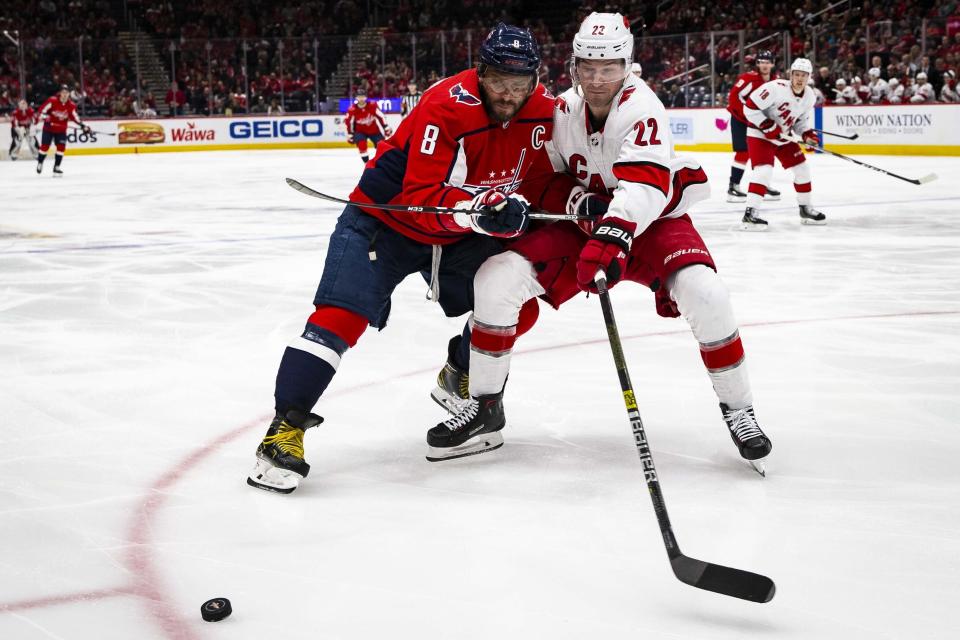 Washington Capitals left wing Alex Ovechkin (8), from Russia, and Carolina Hurricanes defenseman Brett Pesce (22) reach for the puck during the second period of an NHL hockey game, on Monday, Jan. 13, 2020, in Washington. (AP Photo/Al Drago)