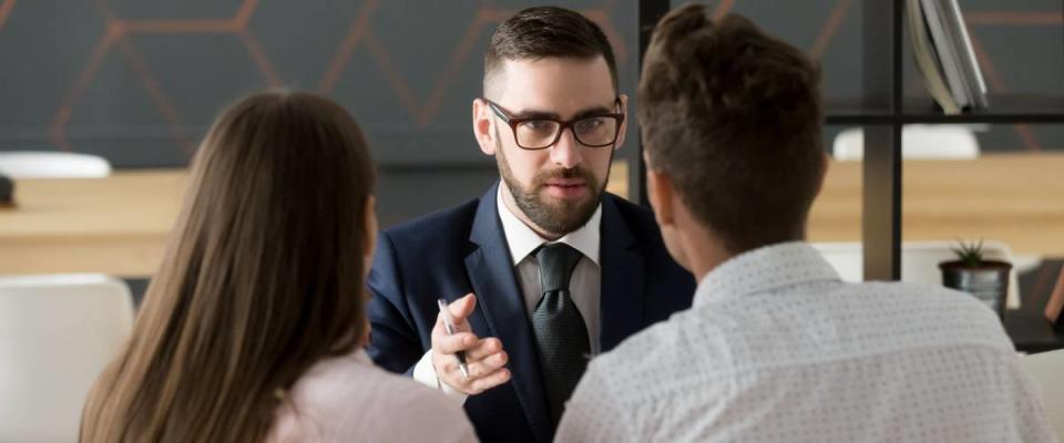 Serious financial advisor in suit and glasses talking to young couple