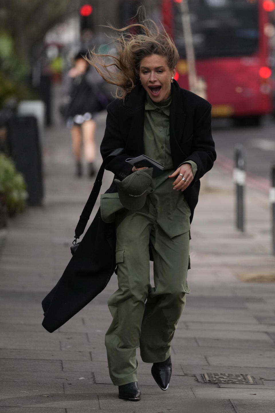 A woman attending a fashion show at London Fashion Week reacts to the wind as she waits to enter the runway presentation in London, Friday, Feb. 18, 2022. Millions of Britons are being urged to cancel travel plans and stay indoors Friday amid fears of high winds and flying debris as the second major storm this week prompted a rare "red" weather warning across southern England (AP Photo/Alastair Grant)