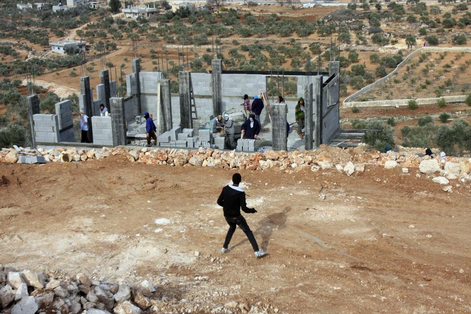 Palestinians throw stones at Israeli settlers who are later detained by Palestinian villagers in a building under construction near the West Bank village of Qusra, southeast of the city of Nablus, Tuesday, Jan. 7, 2014. Palestinians held more than a dozen Israeli settlers for about two hours Tuesday in retaliation for the latest in a string of settler attacks on villages in the area, witnesses said. The military said the chain of events apparently began after Israeli authorities removed an illegally built structure in Esh Kodesh, a rogue Israeli settlement in the area. In recent years, militant settlers have often responded to any attempts by the Israeli military to remove parts of dozens of rogue settlements, or outposts, by attacking Palestinians and their property. The tactic, begun in 2008, is known as "price tag." (AP Photo/Nasser Ishtayeh)