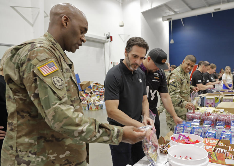 FILE - In this May 14, 2019, file photo, NASCAR driver Jimmie Johnson, second from left, helps assemble care packages for the North Carolina USO during a news conference in Concord, N.C. NASCAR's nicest guy will run his final race this week and close a remarkable career. Jimmie Johnson's record-tying seven Cup titles are well celebrated, but his charitable work goes less noticed. The Jimmie Johnson Foundation has donated more than $12 million to schools and programs since it launched. (AP Photo/Chuck Burton, File)