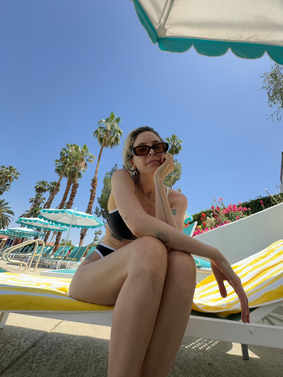 Person lounging on a poolside chair with palm trees in the background, indicative of a sunny vacation spot