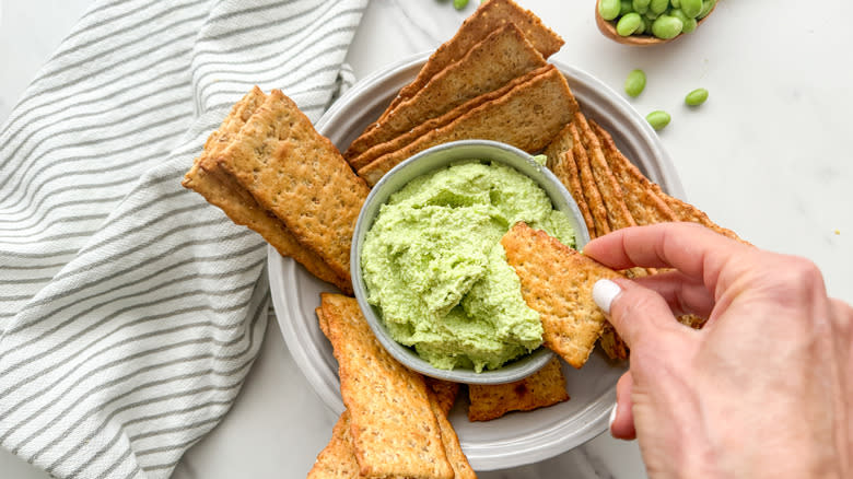 hand dipping cracker in hummus