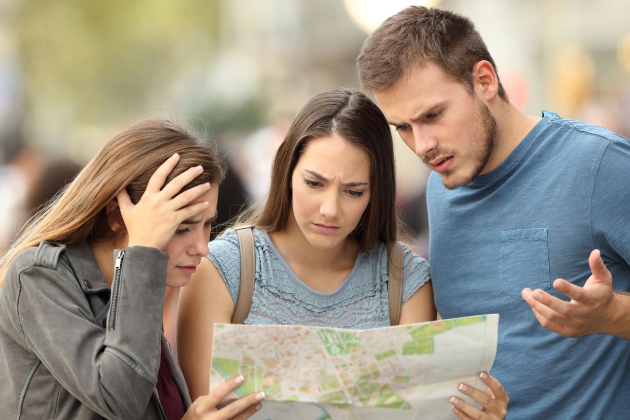 Three worried lost tourists trying to find a location in a paper map on the street
