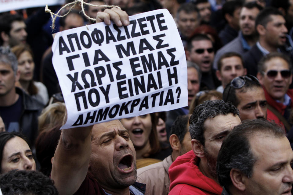 A protestor holds a banner that reads in Greek "You decide for us without us, where’s the democracy in that?" outside of the Parliament during a strike to protest government plans to privatize state-run organizations in Nicosia, Cyprus, Thursday, Feb. 27, 2014. Hundreds of protesters have gathered outside Cyprus' parliament to voice opposition against legislation that will pave the way for the privatization of state-owned companies. (AP Photo/Petros Karadjias)