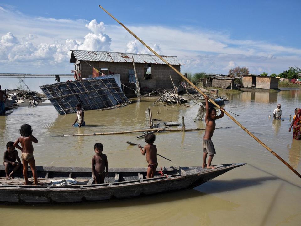 Children row a boat as they pass through damaged houses at a flood-affected village in Morigaon district in the northeastern state of Assam, India. (REUTERS/Anuwar Hazarika)
