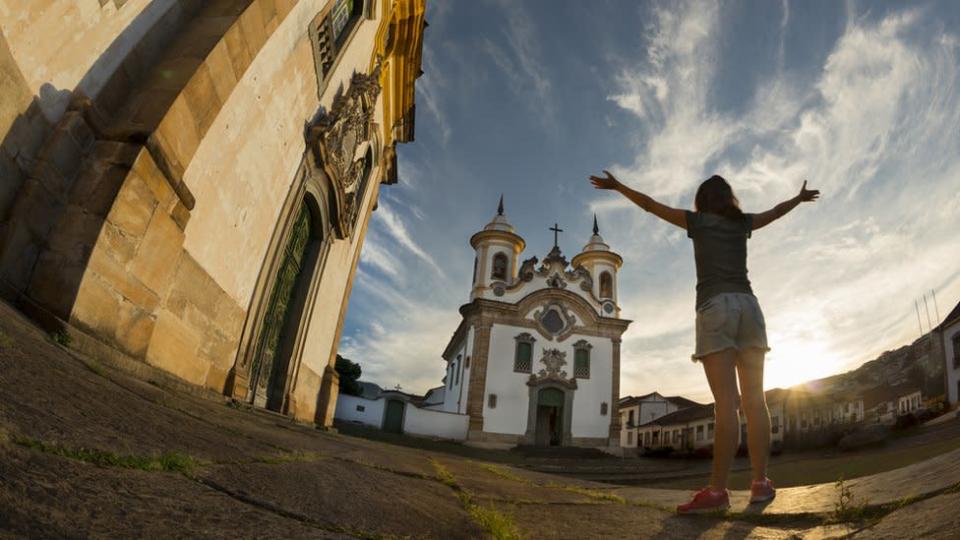 Mulher jovem ao por sol em meio a igrejas em Mariana, Minas Gerais