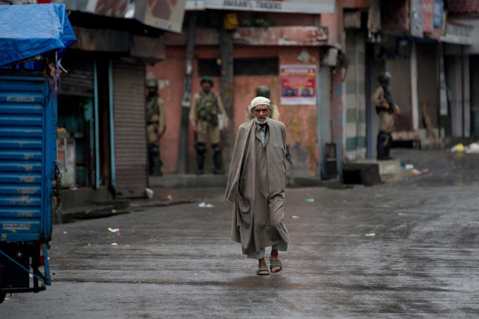 A Kashmiri man walks as Indian paramilitary soldiers stand guard during security lockdown in Srinagar on Aug. 14, 2019.