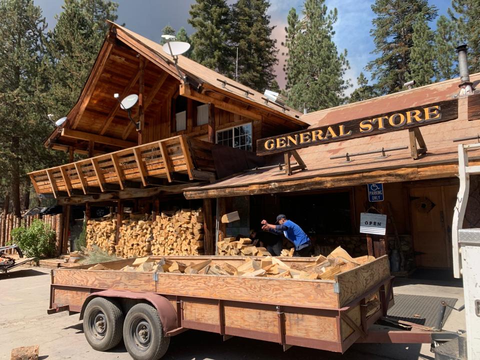 Employees at the Ponderosa Lodge lode up a hauler with the winter's firewood as the Windy Fire climbs up Slate Mountain just west of the town.