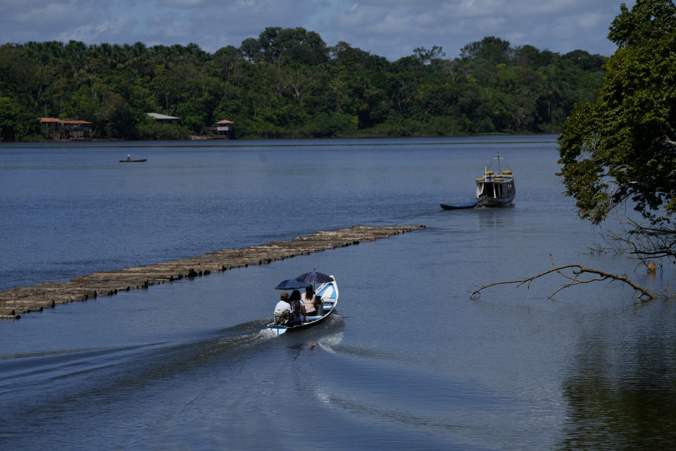 A family travels in a boat shaded by umbrellas next to a boat transporting wooden logs in a section of the Tocantis River, next the island of Tauare, in the municipality of Mocajuba, Para state, Brazil, Friday, June 2, 2023. (AP Photo/Eraldo Peres)