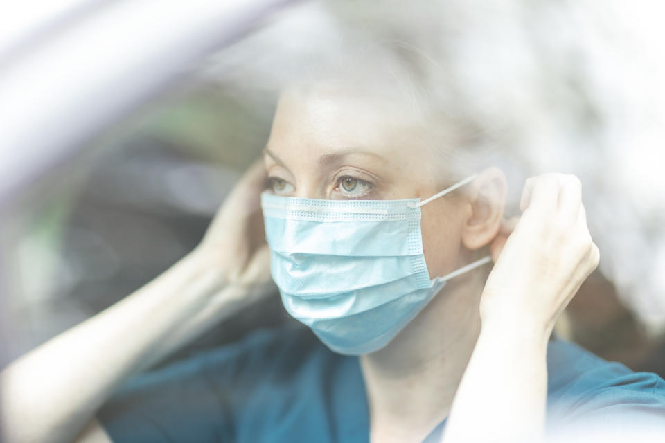 Female community nurse putting on protective mask in car.