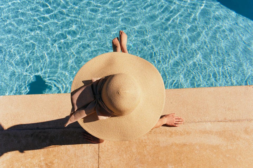 Woman in hat lies near the pool, bright sun