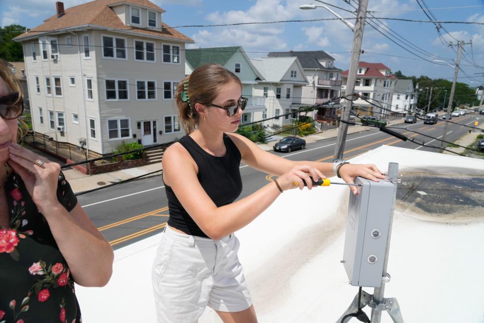 Grace Berg, coordinator of the Breathe Providence project, unscrews the cover on an air quality monitor installed on the roof of the Child & Family Rhode Island building on Eddy Street. Atmospheric chemist Meredith Hastings is at left.