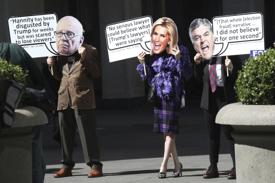 Protesters hold signs depicting Fox News hosts.