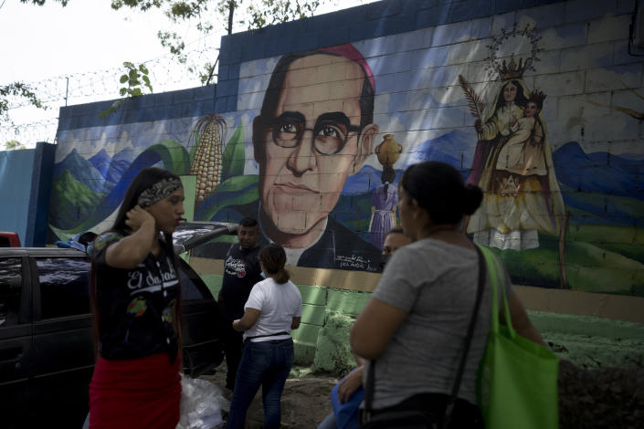Relatives providing food and personal items to family members detained under the ongoing "state of exception", wait next to a mural depicting the late Archbishop Oscar Arnulfo Romero and the Virgin Mary as Our Lady of Peace on an exterior wall of a detention center in Soyapango, El Salvador, Friday, Oct. 7, 2022. (AP Photo/Moises Castillo)