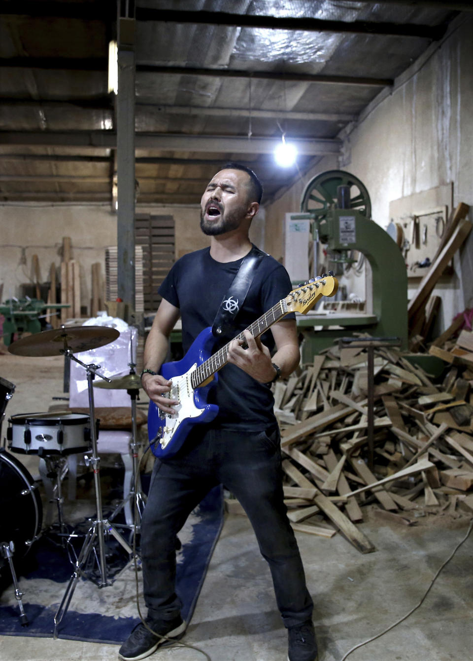 In this July 20, 2018 photo, Afghan musician Hakim Ebrahimi, a member of the Arikayn rock band, sings as he plays guitar at a furniture workshop in Eslamshahr, outside Tehran, Iran. Like others in Iran's vibrant arts scene, Afghan musicians must contend with hard-liners who view Western culture as corrupt and object to women performing in public. (AP Photo/Ebrahim Noroozi)