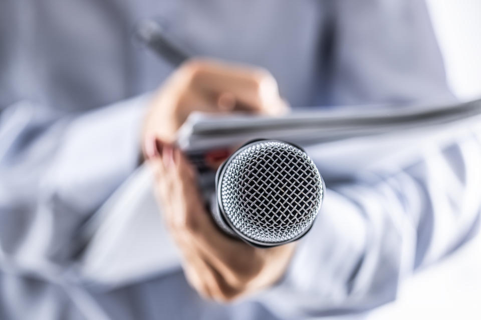 A journalist holds a microphone at a press conference and writes information in a notebook