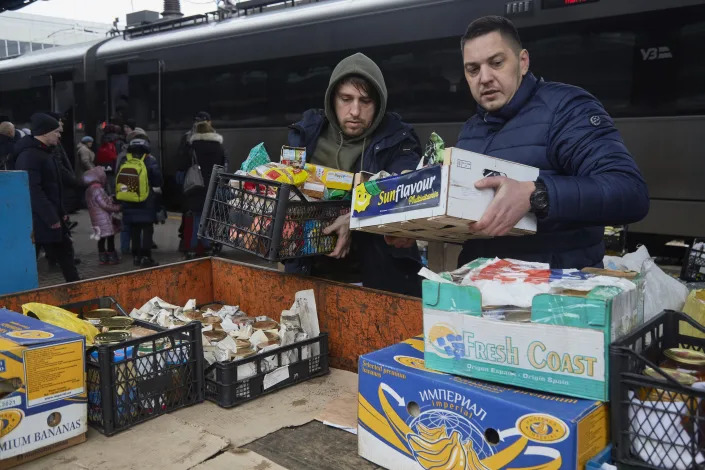 Two men at a train station prepare boxes of food to give away. 