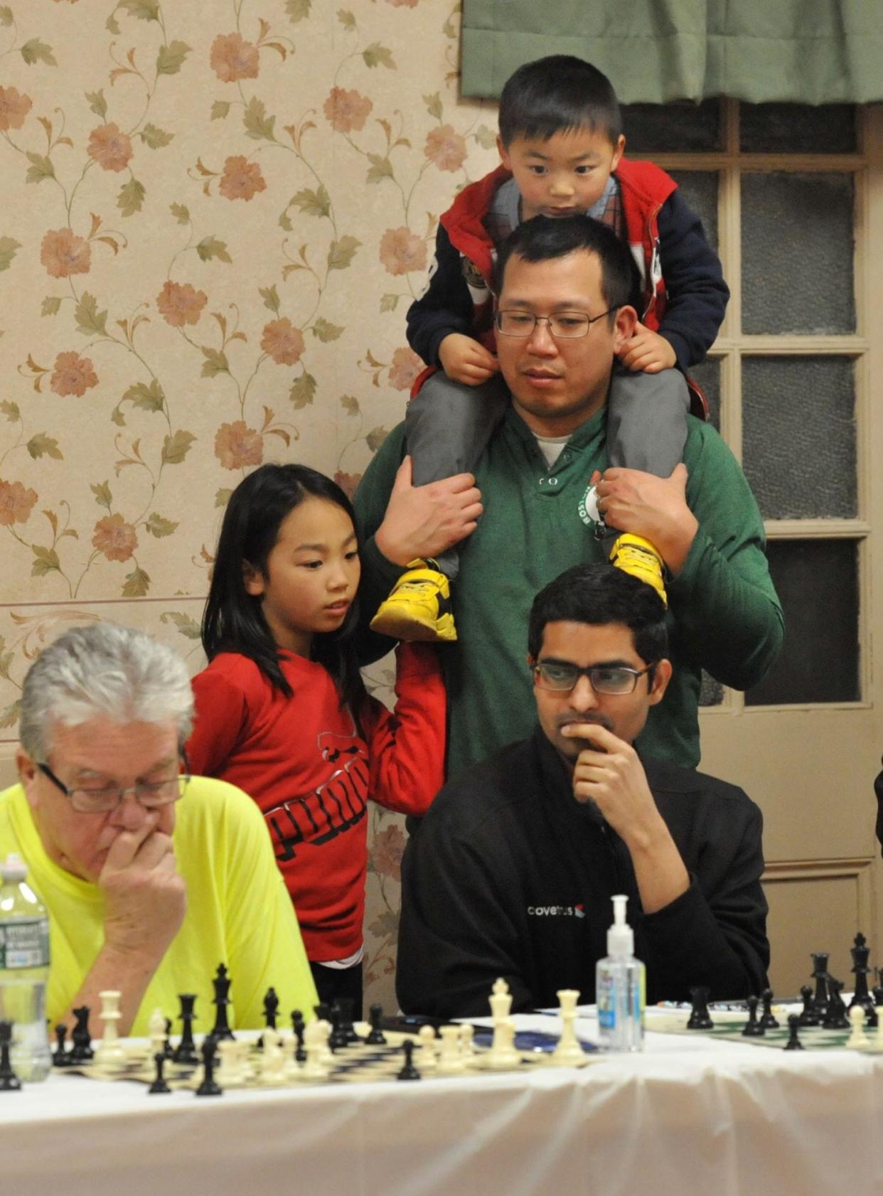 Watching the competition with chess Grandmaster Nadya Kosintseva are Vincent Yu, standing, with his children Kira, 8, second from left, and Eliot, 6, top, at the South Shore Chess Club in Quincy, Wednesday, March 27, 2024.