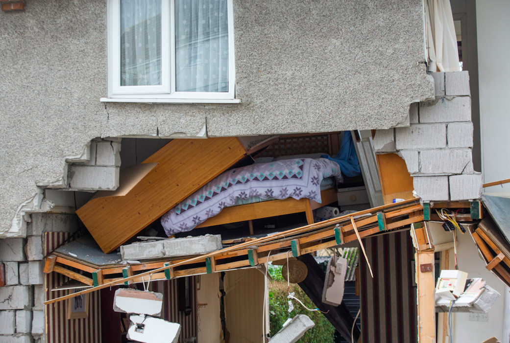 A double bed is exposed to the street from an upper floor room hanging precariously after the support collapsed below. (SWNS)